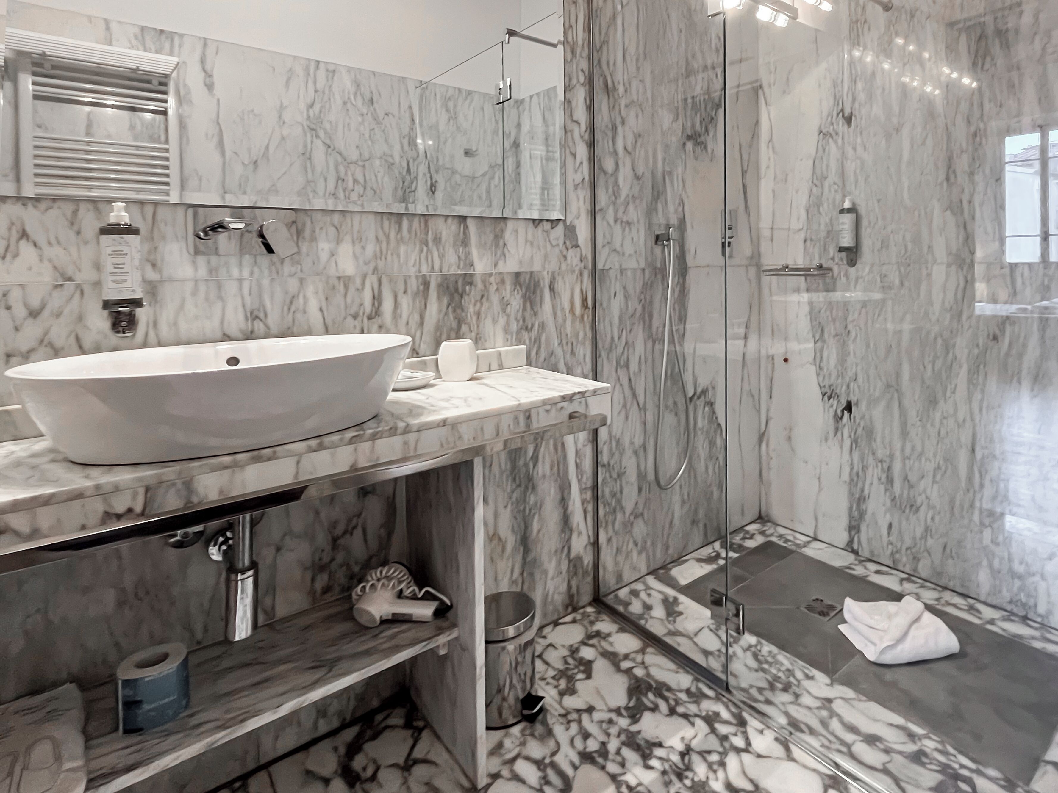 Un baño moderno con un lavabo blanco de diseño, mampara de vidrio y paredes de mármol.