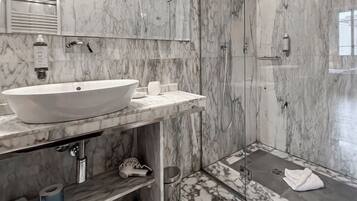 Un baño moderno con un lavabo blanco de diseño, mampara de vidrio y paredes de mármol.