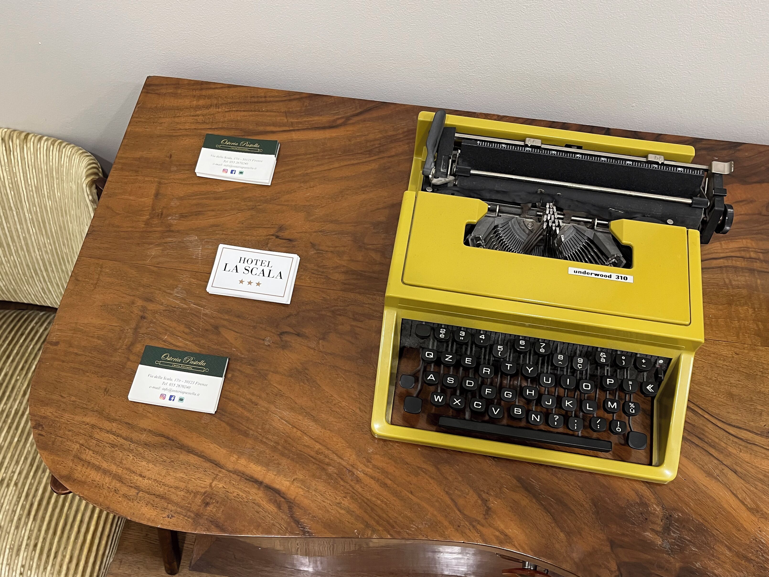 A yellow Underwood 310 typewriter on a wooden table with two business cards labeled "Hotel La Scala" and "Osteria La Scala."