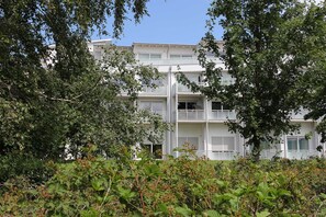 Un immeuble à plusieurs étages doté de balcons, entouré d’une végétation luxuriante.