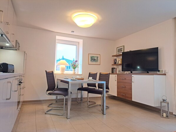 A modern kitchen with a dining table, chairs, a TV, and a window with a view.