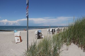 Une plage avec des transats, un ballon de plage et un panneau indicateur.