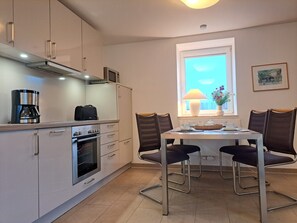A compact kitchen with modern appliances, a dining table with chairs, and a window with a view.
