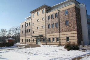 A multi-story building with a brick facade, a covered entrance, and a parking area with snow.