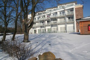 Un immeuble à plusieurs étages doté de balcons, d’une façade en briques et d’un sol recouvert de neige.