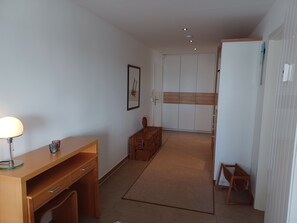 Une pièce avec un bureau en bois, une lampe, un tableau encadré, une armoire et un petit tabouret en bois.