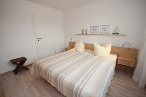 Une chambre à coucher comprenant un lit, des tables de chevet, une commode, un plancher en bois, une porte et une étagère avec des photos encadrées.
