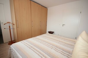 A bedroom with a bed, wooden wardrobe, and a hanging coat rack.