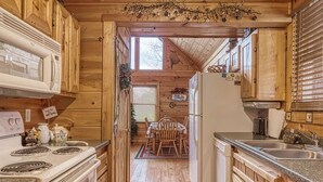 Une cuisine rustique, située dans une cabane en bois, équipée d’un poêle, d’un réfrigérateur et de meubles de rangement en bois.