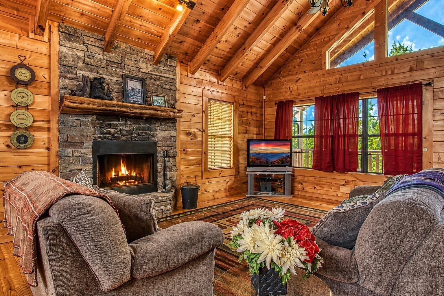 A cozy cabin interior with a stone fireplace, wooden walls, a television, and two sofas.