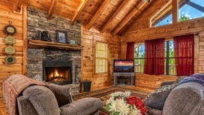 A cozy cabin interior with a stone fireplace, wooden walls, a television, and two sofas.