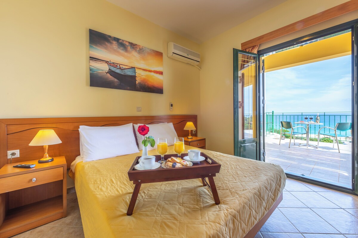 A hotel room with a bed, a tray with breakfast items, a painting on the wall, and a balcony with a view.