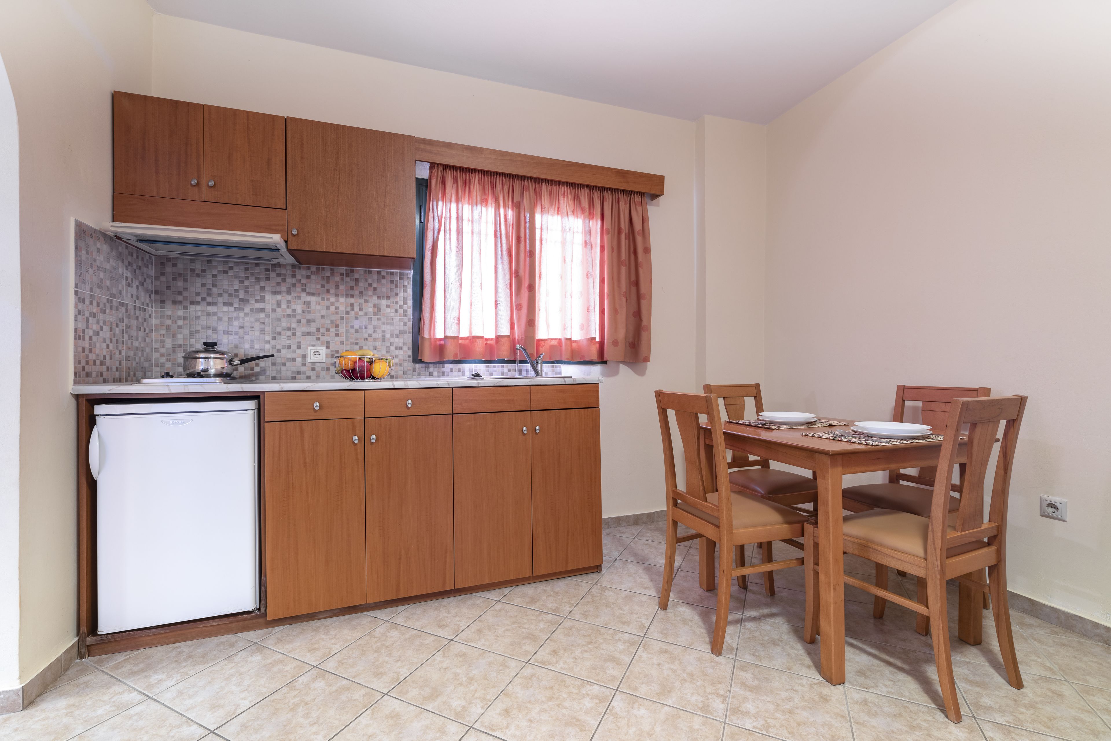 A compact kitchen with wooden cabinets, a built-in oven, a refrigerator, and a dining table with chairs.