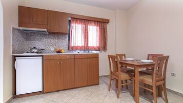 A compact kitchen with wooden cabinets, a built-in oven, a refrigerator, and a dining table with chairs.