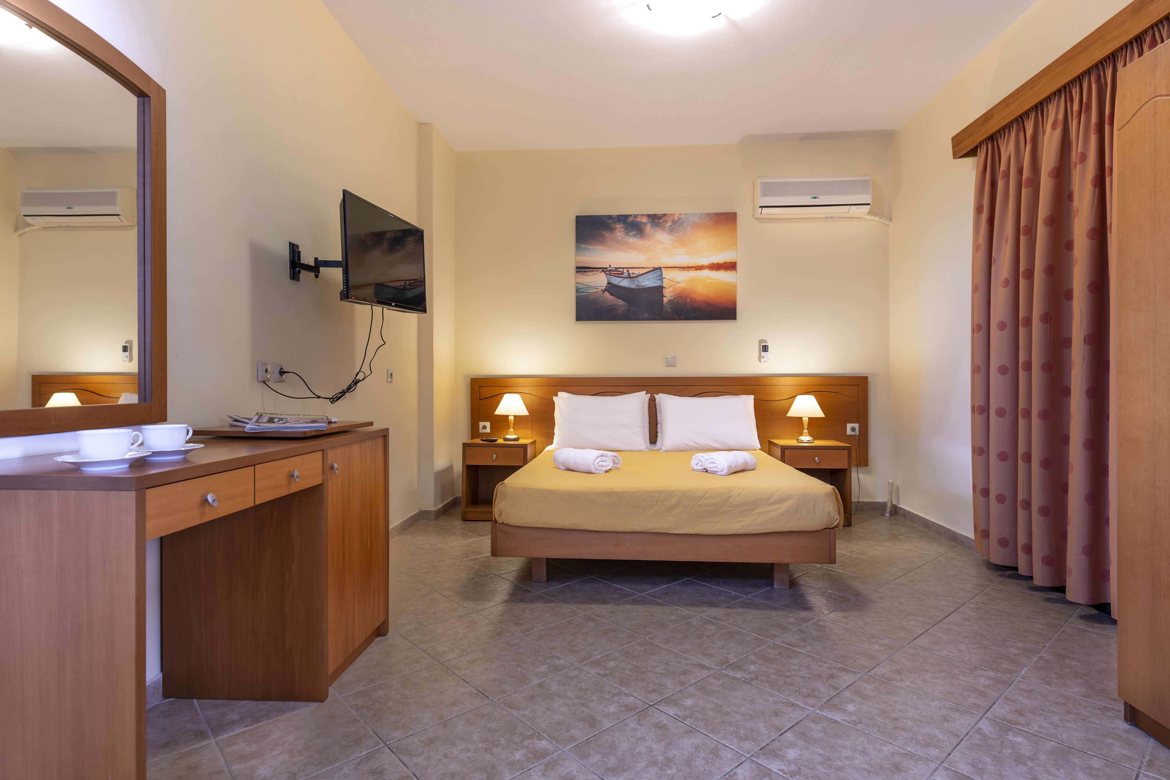 Quarto de hotel com cama, mesas de cabeceira, televisão na parede e um quadro sobre a cama.