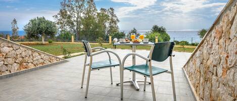 An outdoor seating area with stone walls, a table with chairs, and a view of the sea.