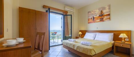 Habitación de hotel con cama, escritorio con tazas, una silla, un cuadro y vistas a través de la puerta abierta.