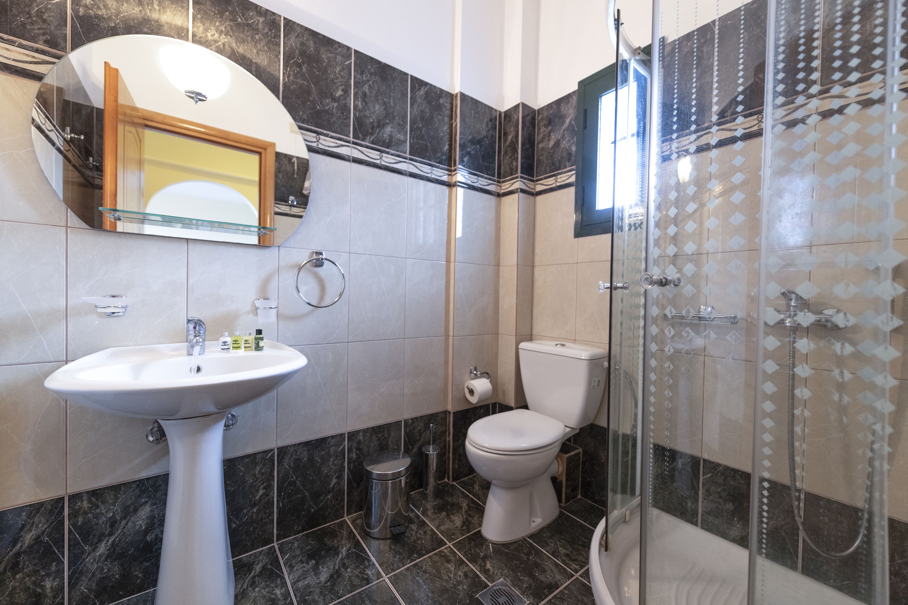 A bathroom with a white sink, a toilet, a glass shower enclosure, and a mirror above the sink.