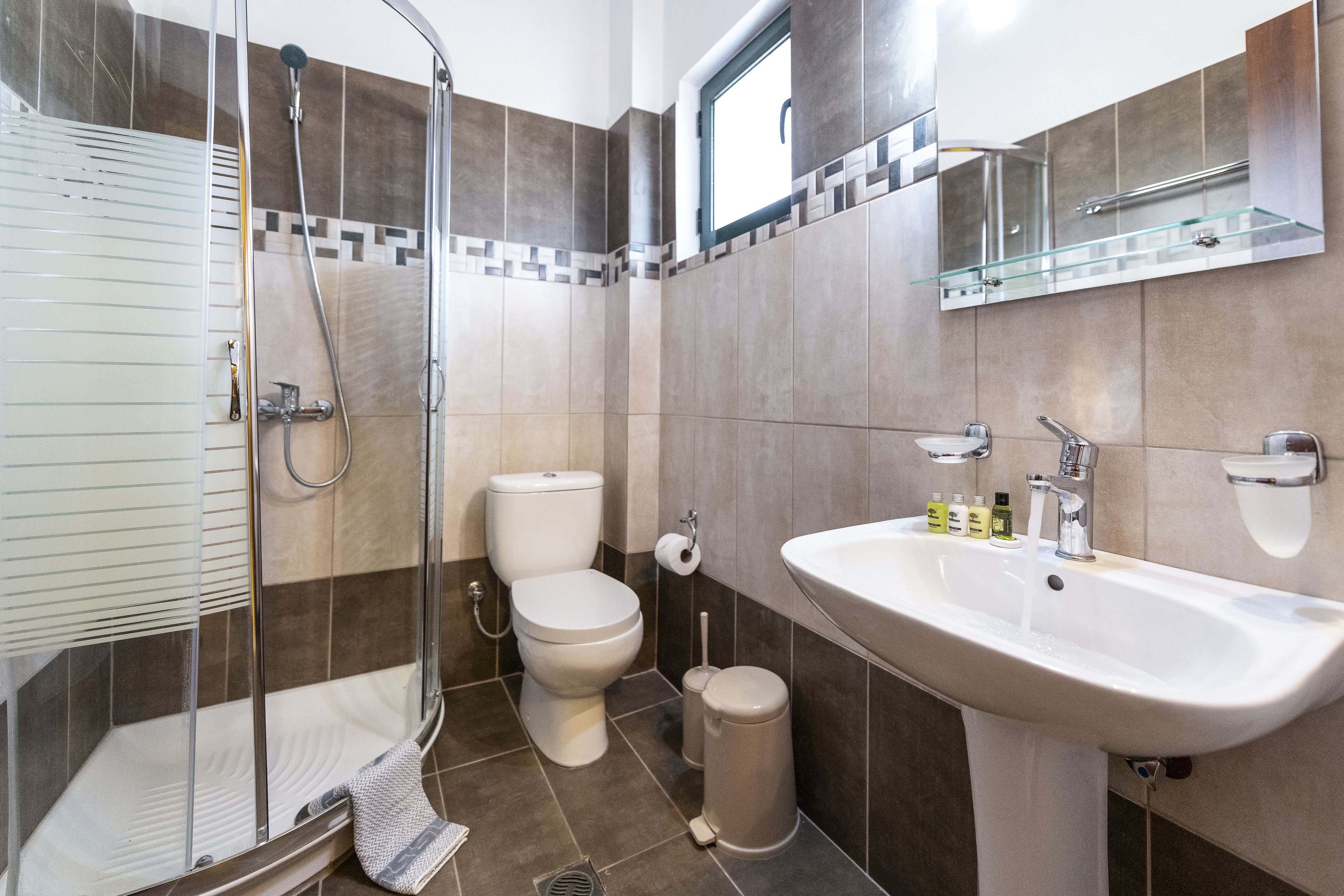 Ein modernes Badezimmer mit Dusche, Toilette, Waschbecken und einem Glasregal darüber.