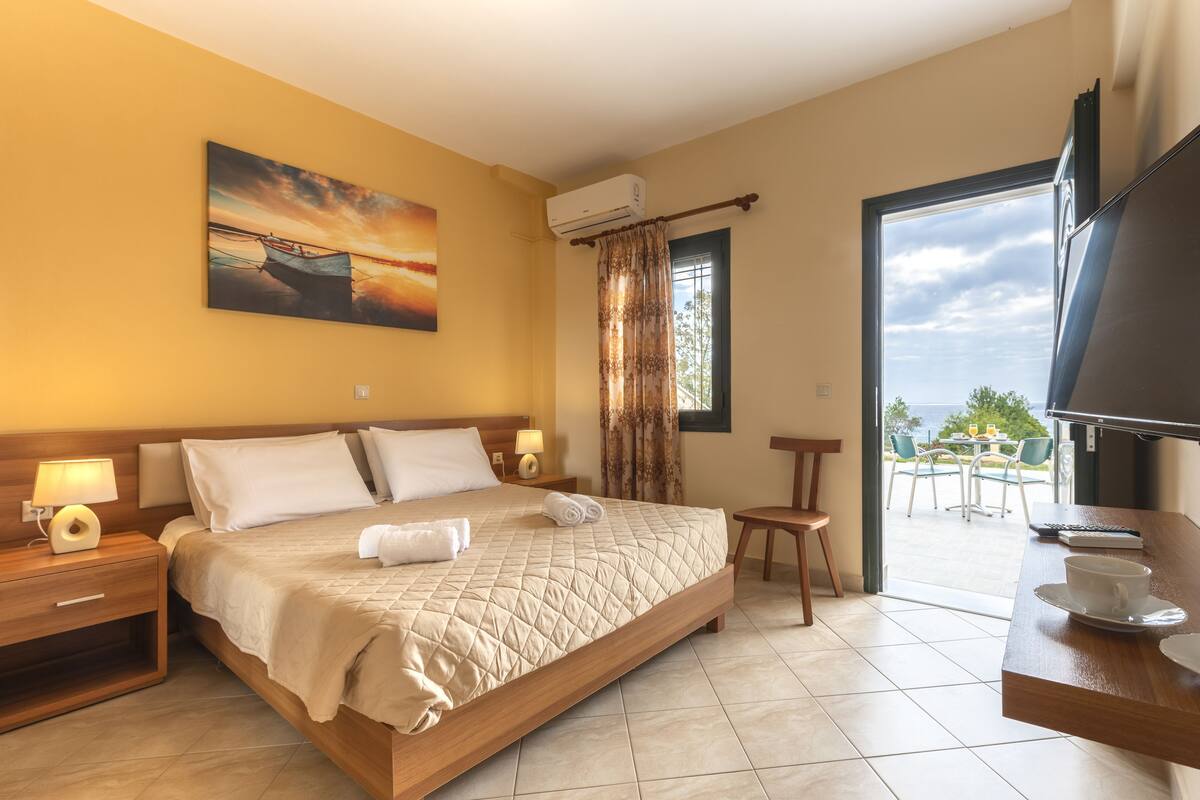 Ein Hotelzimmer mit einem großen Bett, einem Fernseher, einem Balkon mit Tisch und Stühlen sowie einem Bild an der Wand.