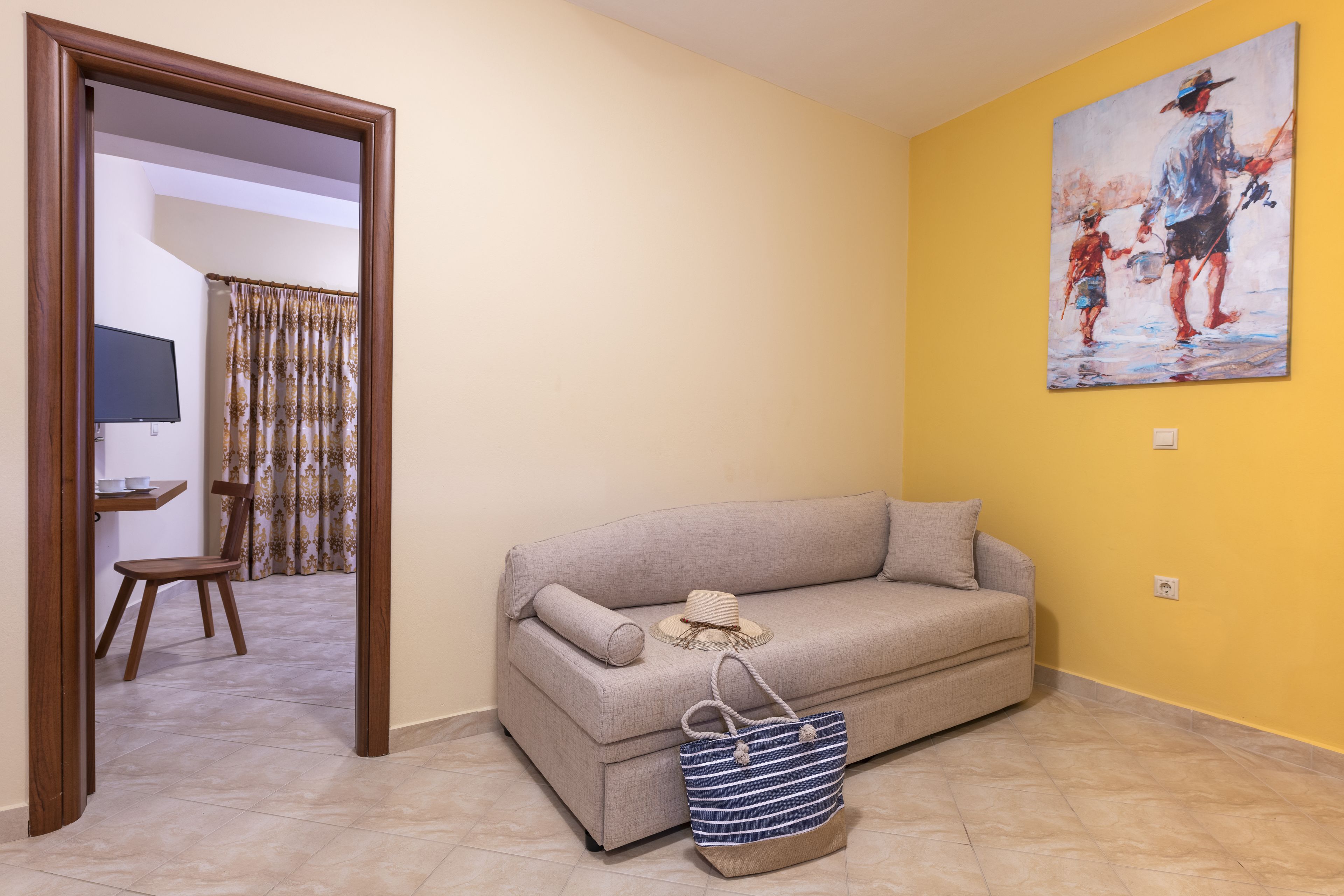 A living room with a sofa, a painting on the wall, and a door leading to another room.