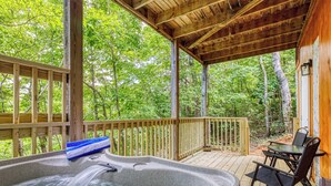 A wooden deck with a hot tub, a table, and chairs, surrounded by trees. - Forever Yours, 2 Hot tubs, FREE Attraction tickets, WIFI, Near The Parkway!!! (Pigeon Forge)
