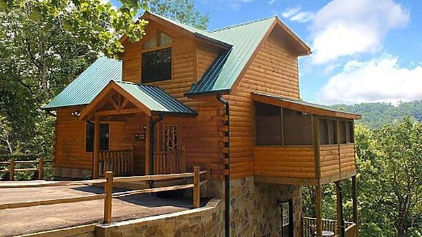A wooden cabin with a stone foundation, a balcony, and a metal roof. - Bearskin Romance- Free Attraction Tickets ,WIFI, Pool Table, Air Hockey, Hot Tub (Sevierville)