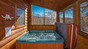 A wooden cabin interior with a hot tub, large windows, and a view of autumn trees. - Bearskin Romance- Free Attraction Tickets ,WIFI, Pool Table, Air Hockey, Hot Tub (Sevierville)