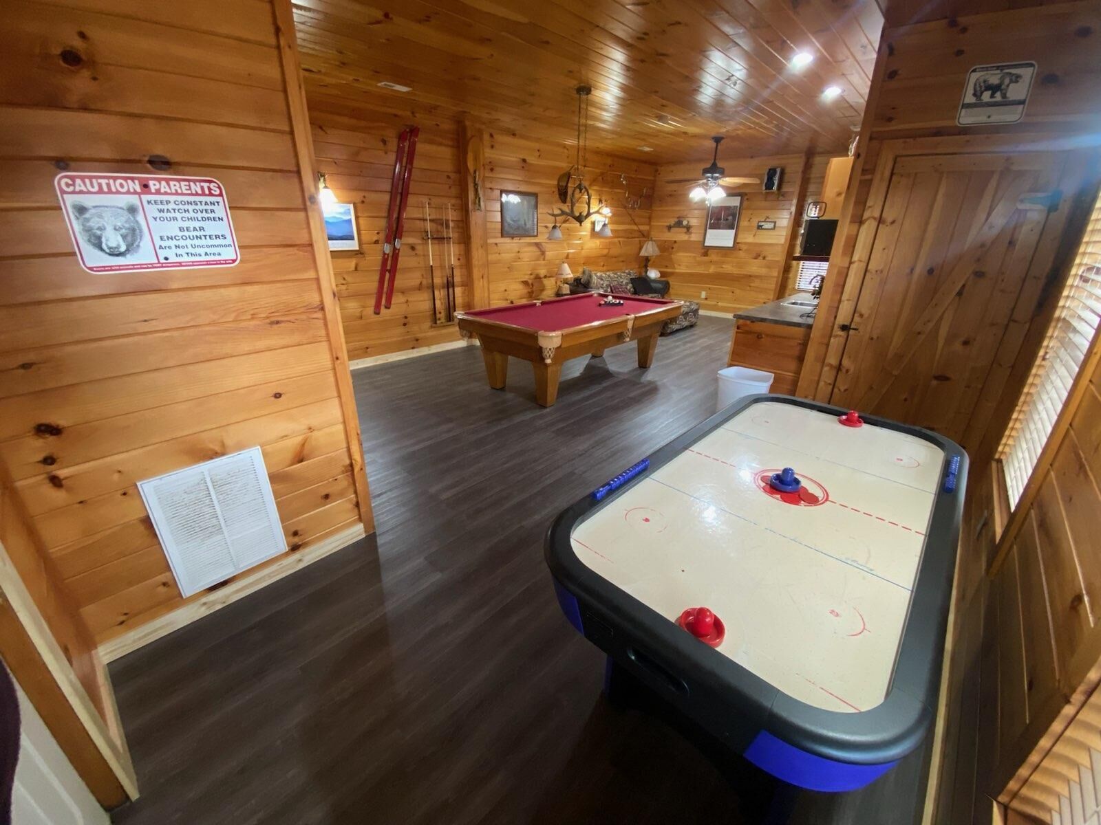 L’intérieur d’un chalet en bois, avec une table de billard, une table de baby-foot et un panneau d’avertissement concernant les risques de rencontre avec des ours.