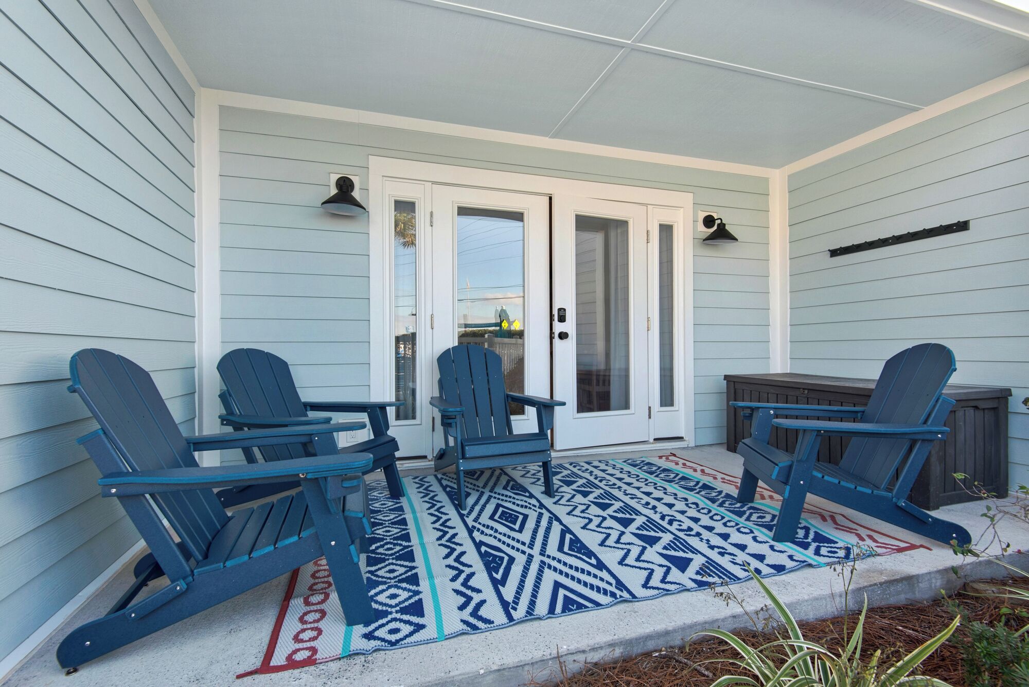 A covered porch with three Adirondack chairs, a small table, and a patterned rug.