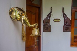Un llamador de bronce con forma de elefante y un cascabel, una puerta de madera y dos esculturas de animales montadas en la pared con un cartel de 'Welcome'.