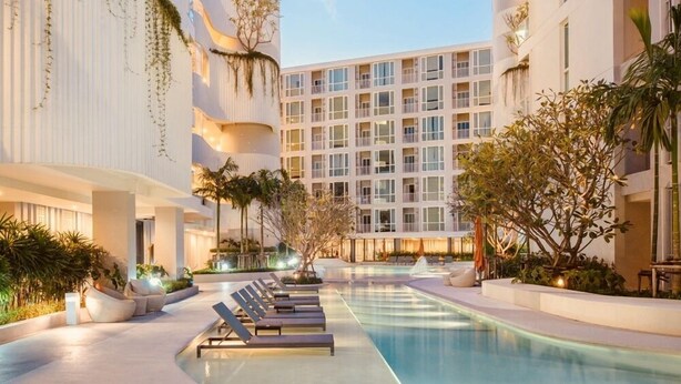 Un hotel moderno con zona de piscina, sillas de descanso y un edificio de varios pisos con balcones.