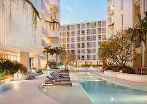 A modern hotel with a pool area, lounge chairs, and a multi-story building with balconies. - The Base Downtown Condo by Joy (Wichit)