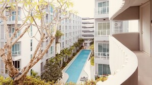 Un hotel moderno con piscina central, rodeado de exuberante vegetación y balcones blancos.