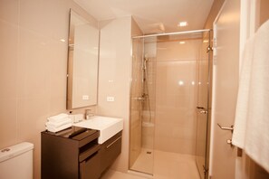 A modern bathroom with a glass-enclosed shower, a white sink, and a large mirror. - The Base Downtown Condo by Joy (Wichit)