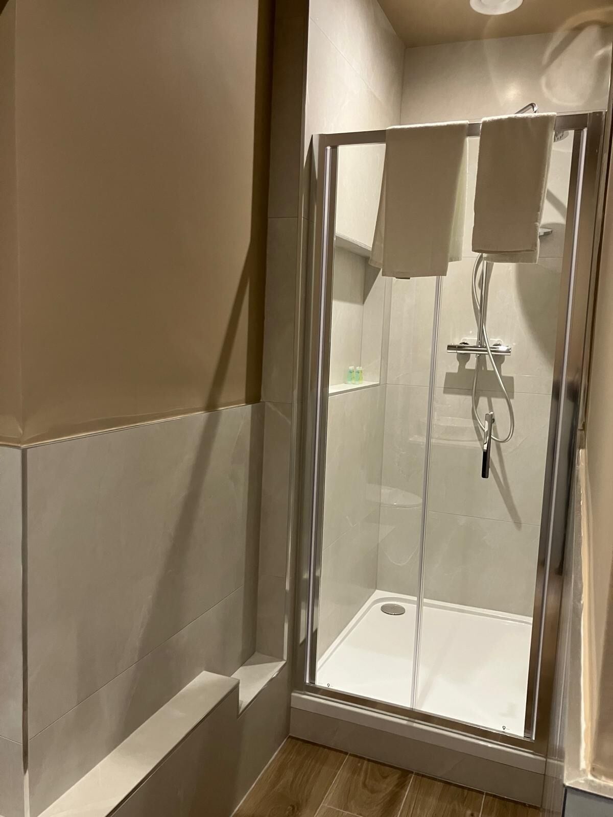 A glass-enclosed shower with a white interior, a towel rack, and a shelf with toiletries.