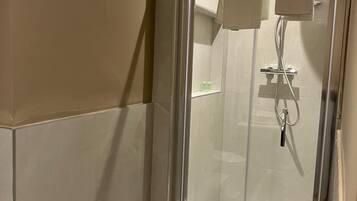 A glass-enclosed shower with a white interior, a towel rack, and a shelf with toiletries.