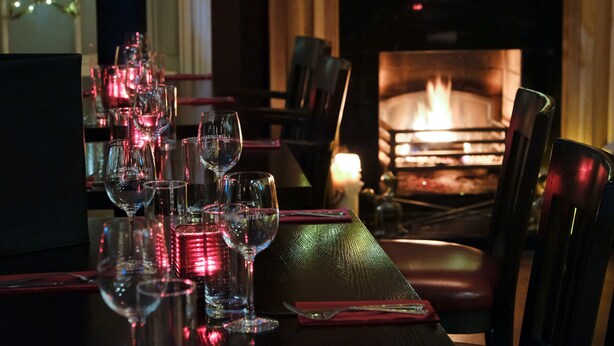 A dining table set with multiple wine glasses and red napkins, a lit candle, and a fireplace in the background. - The Horse & Hound (Delgany)