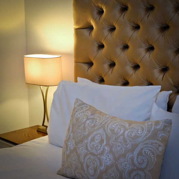A bed with white bedding and a patterned pillow, a tufted headboard, and a bedside lamp. - The Horse & Hound (Delgany)