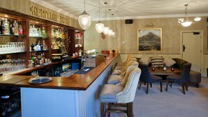A bar area with a long counter, multiple hanging light fixtures, and a seating area with a table and chairs. - The Horse & Hound (Delgany)