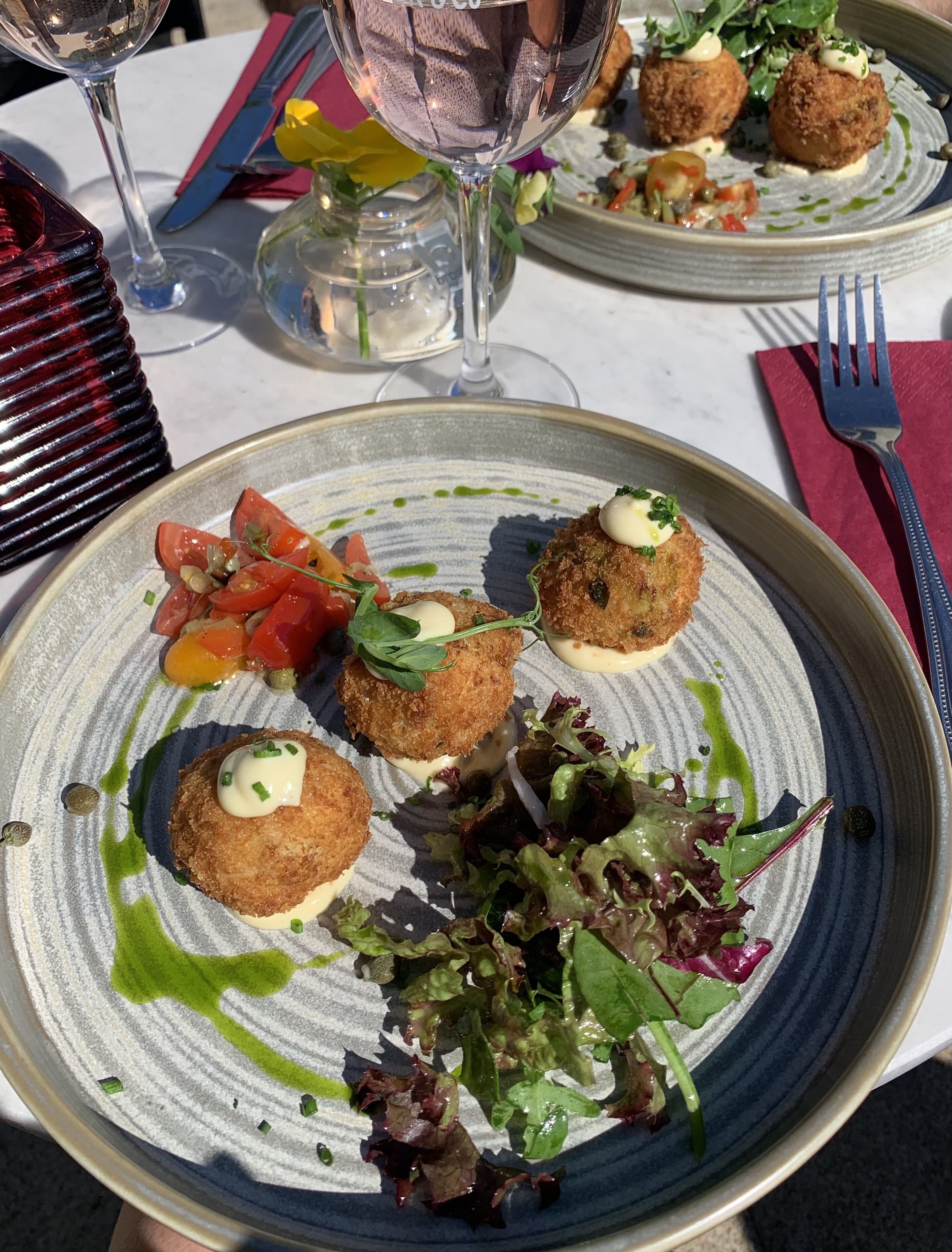 A dining table with plates of food, a wine glass, and a vase with flowers.