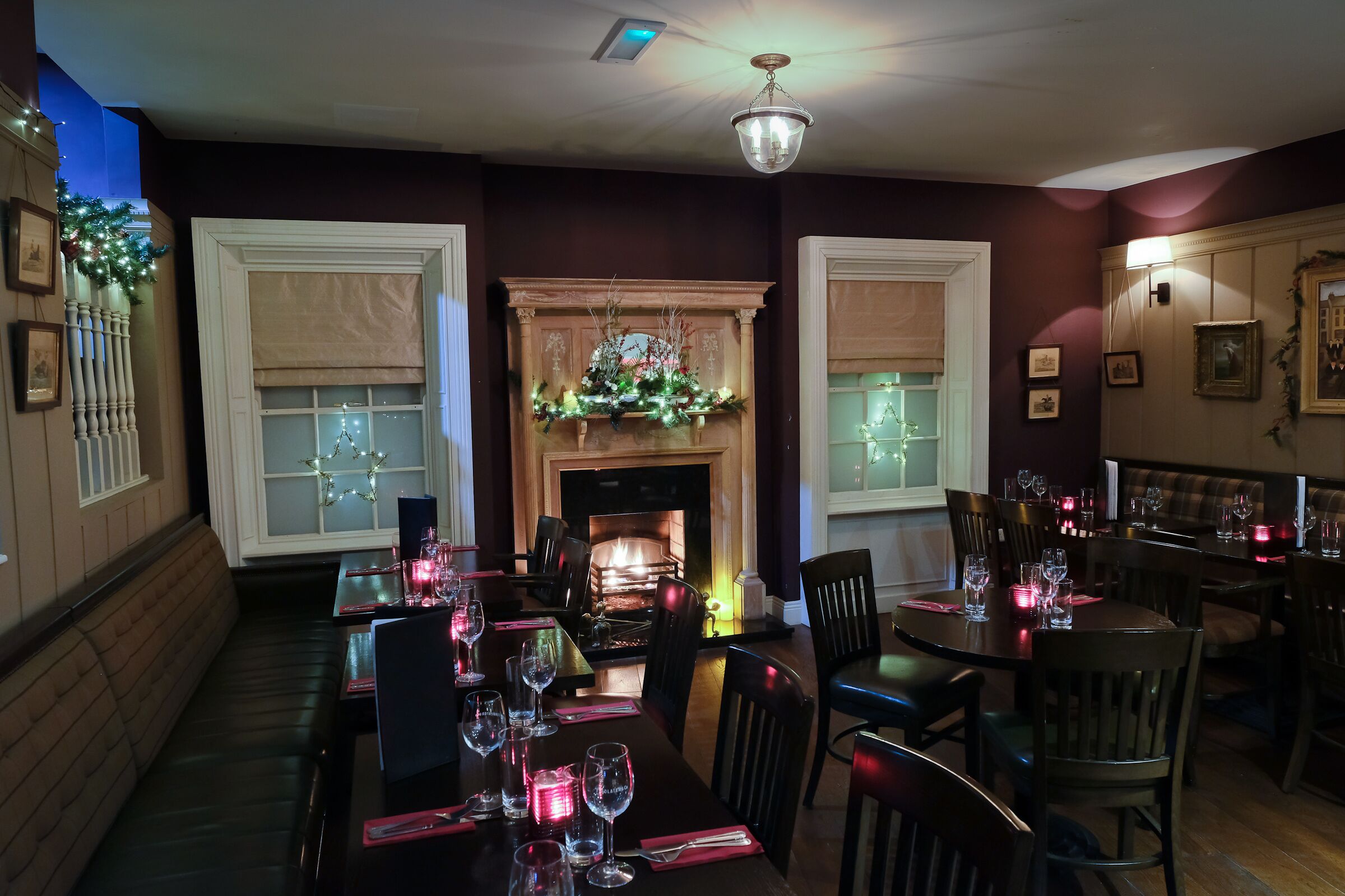 Un comedor con mesas dispuestas para una comida, una chimenea y decoraciones navideñas.