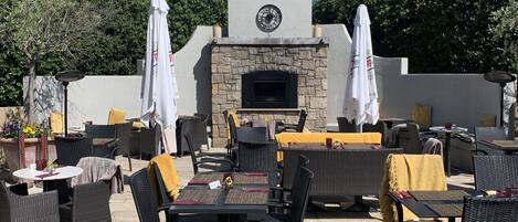 Une terrasse extérieure avec un sol carrelé en pierre, des meubles en rotin noir et des parasols blancs.