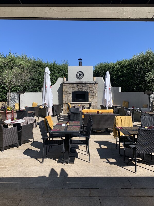An outdoor patio with stone-tiled flooring, black wicker furniture, and white umbrellas. - The Horse & Hound (Delgany)
