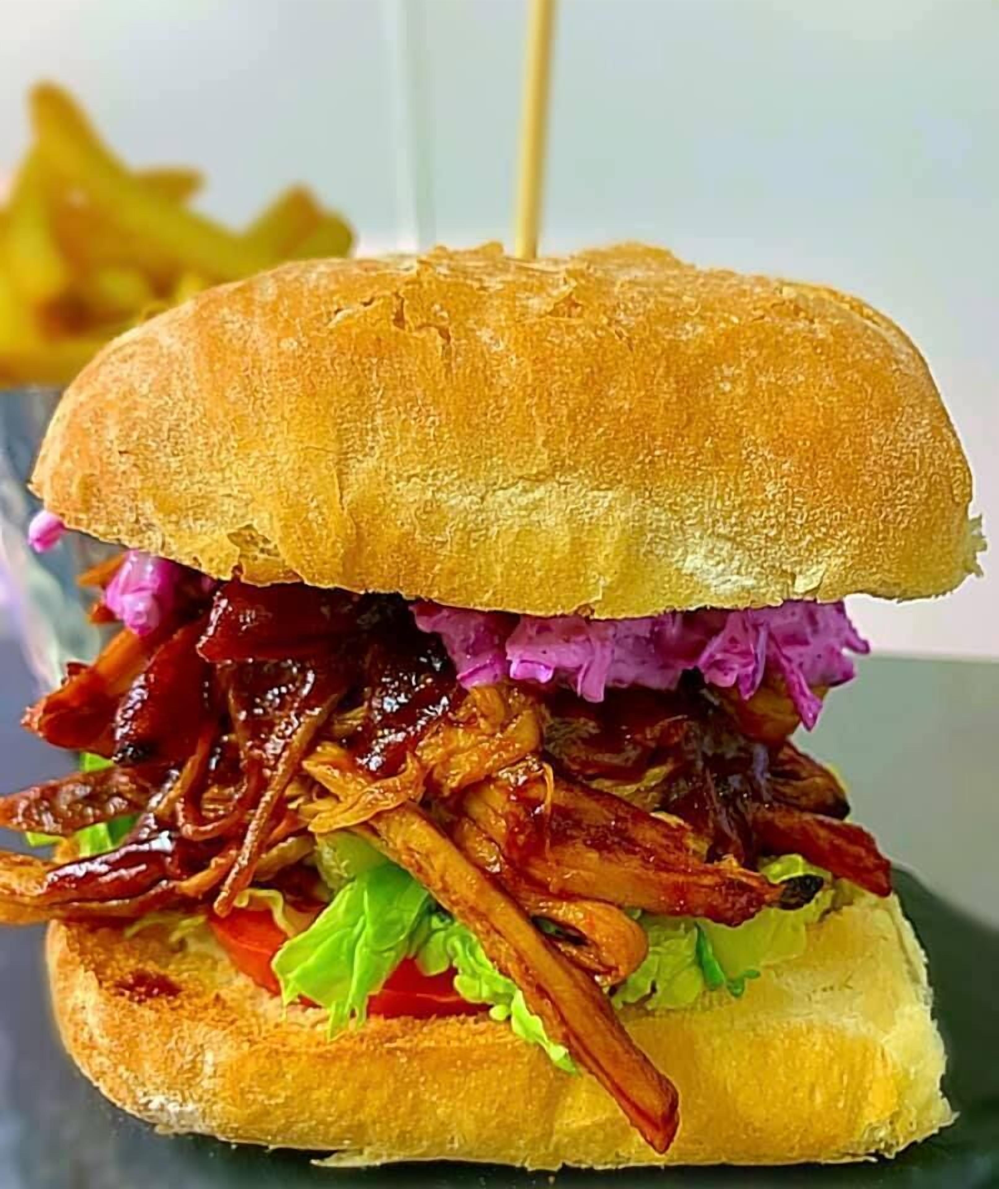Ein Sandwich mit gegrilltem Brötchen, gezupftem Schweinefleisch, Rotkohl und Salat.