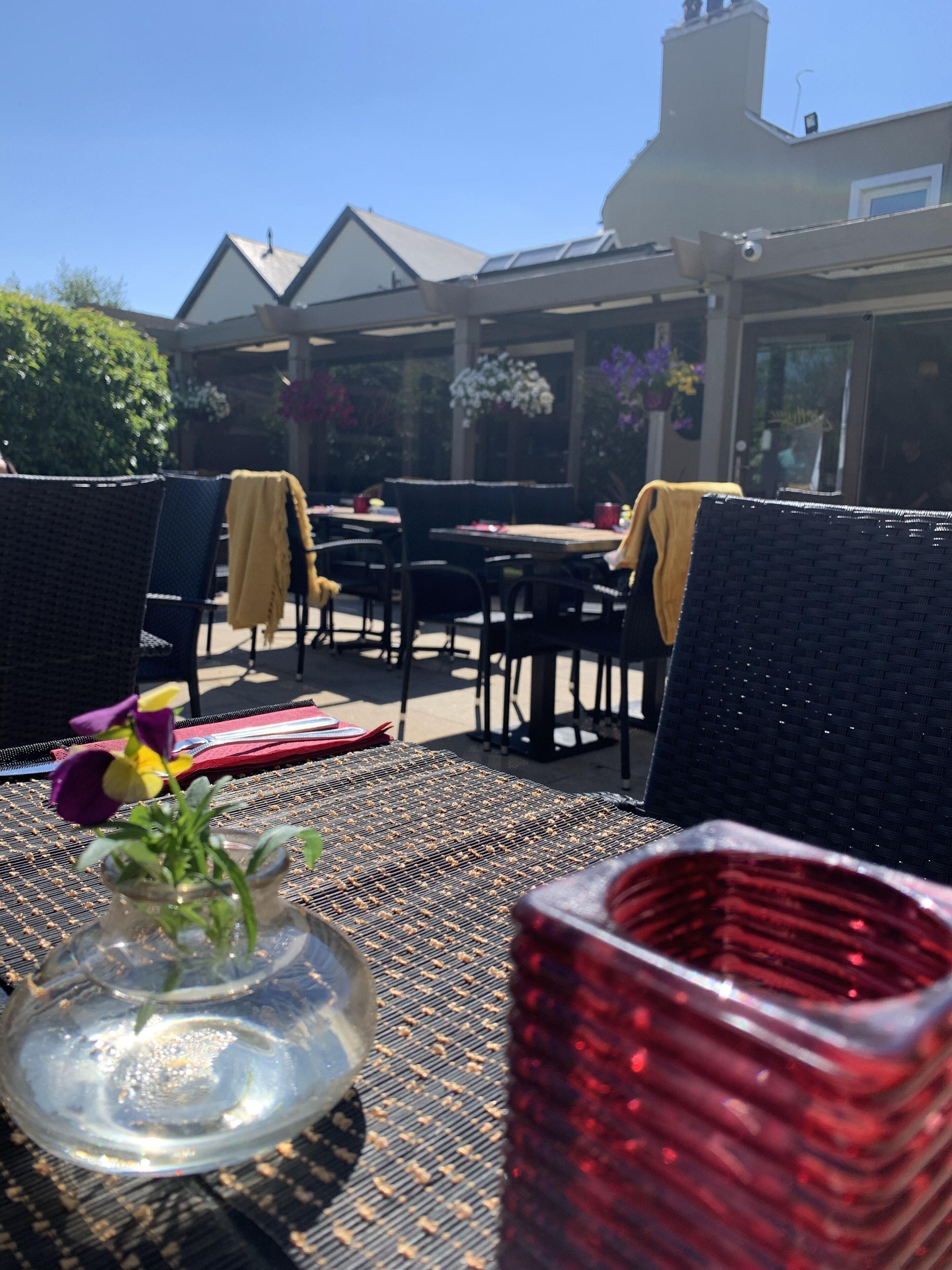 An outdoor patio with wicker furniture, a glass vase with flowers, and a red decorative item.