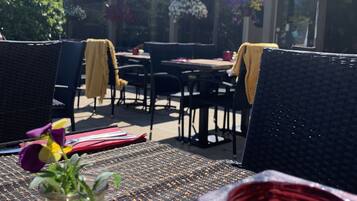 An outdoor patio with wicker furniture, a glass vase with flowers, and a red decorative item.