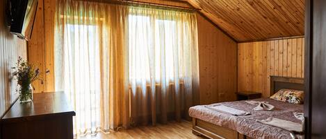 A wooden-paneled room with a bed, a nightstand, and a TV mounted on the wall.