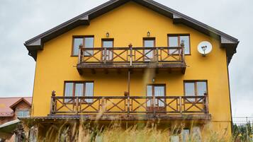 Two-story building with a balcony and satellite dish, set amidst lush surroundings.