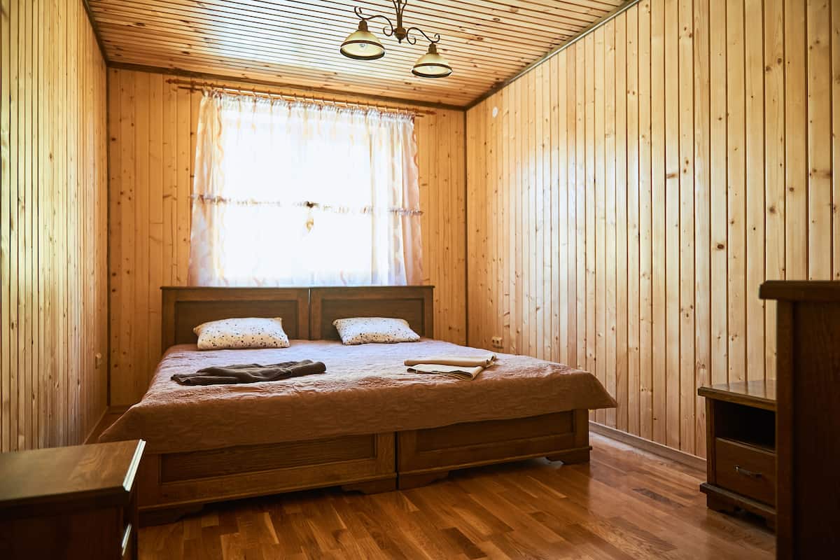 Una habitación con paneles de madera, una cama, una mesita de noche y un armario pequeño.